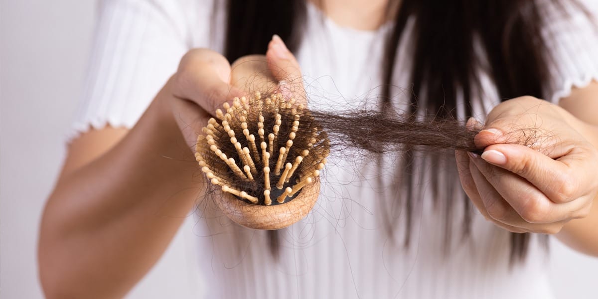 Lady pulling hair out of her brush, suffering from hair loss