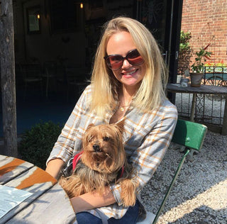 A blonde lady with sunglasses sitting and holding a dog.